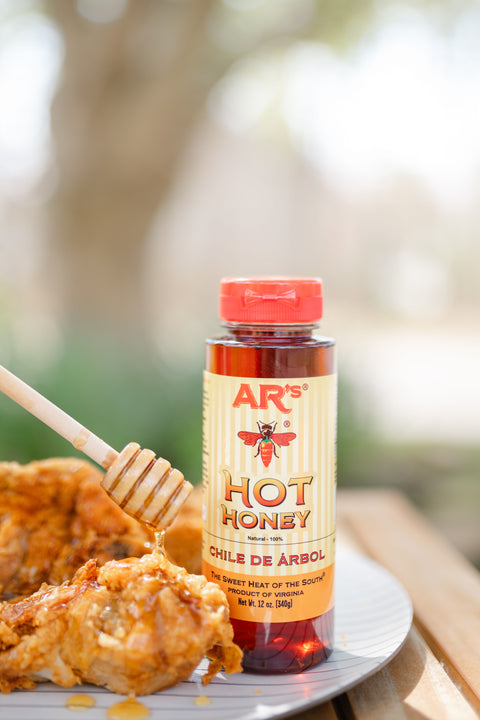 Bottle of AR's Hot Honey with fried chicken on a plate outdoors